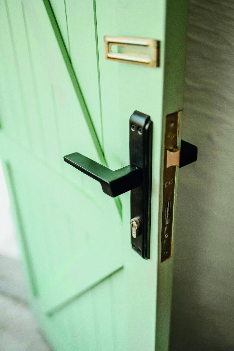 A black lever handle and mortise lock on a mint-green door