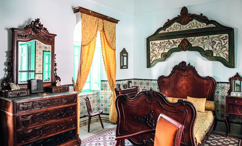 A heritage-style bedroom with carved wooden furniture, patterned tiles and yellow drapes