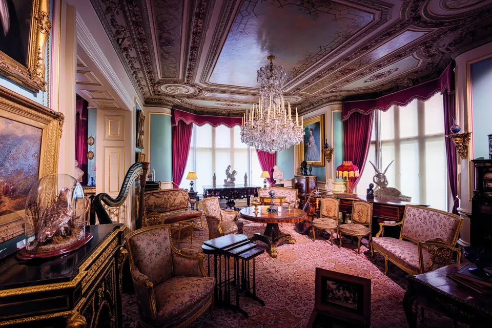 A Victorian drawing room with an ornate ceiling, crystal chandelier and antique furniture